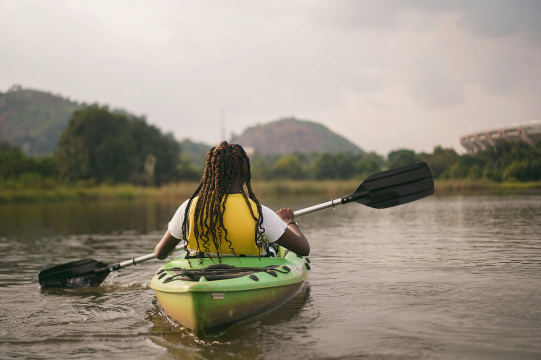 A person sitting in a green kayak wearing a yellow life jacket and are rowing into the distance.