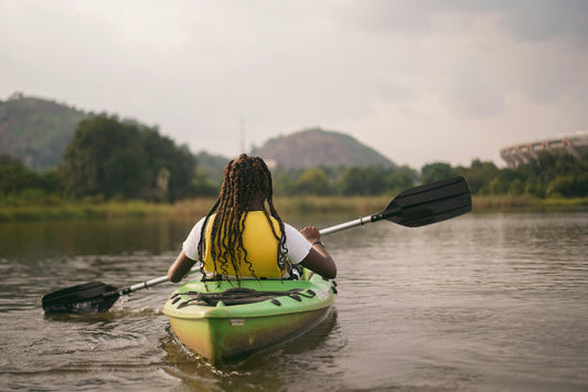 A person sitting in a green kayak wearing a yellow life jacket and are rowing into the distance.
