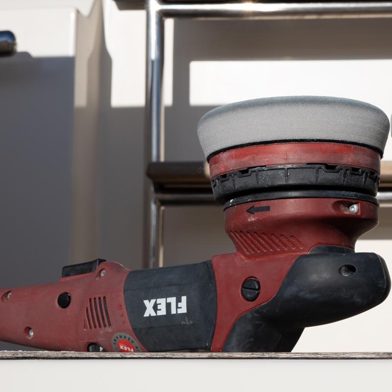A close-up image of a FLEX orbital polishing machine with a foam pad, placed on a surface with a boat's railing in the background. The tool is positioned with the foam pad visible, showing its detailed construction and design.