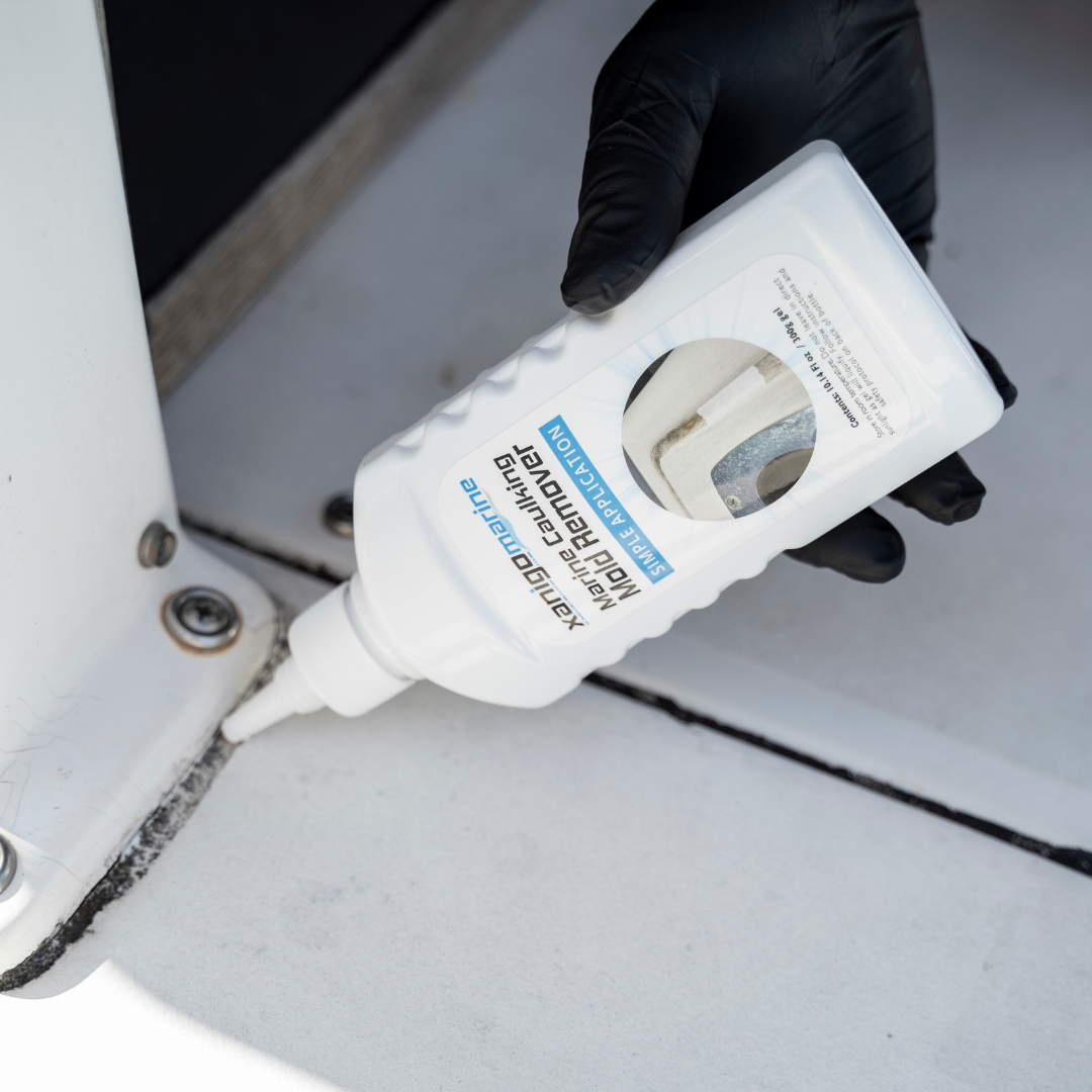 A person wearing a black glove applying Xanigo Marine Caulking Mold Remover to a boat's caulking. The bottle, featuring the product label, is shown as the mold remover is being dispensed onto the surface for effective cleaning.