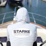 A person wearing a light-colored hoodie with the 'STARK' logo on the back, sitting on the deck of a yacht, overlooking the water and docks.