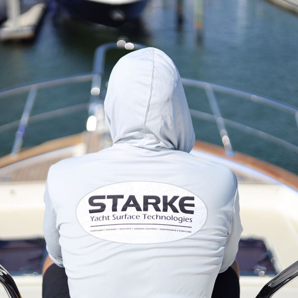 A person wearing a light-colored hoodie with the 'STARK' logo on the back, sitting on the deck of a yacht, overlooking the water and docks.